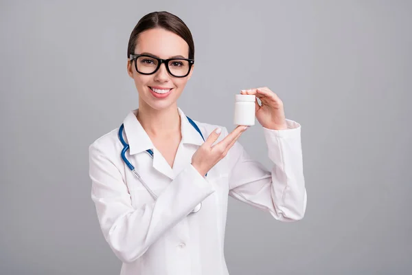 Фото чарівної позитивної молодої леді лікар робочий одяг окуляри посміхаючись тримає пляшку таблеток ізольований сірий колір фону — стокове фото