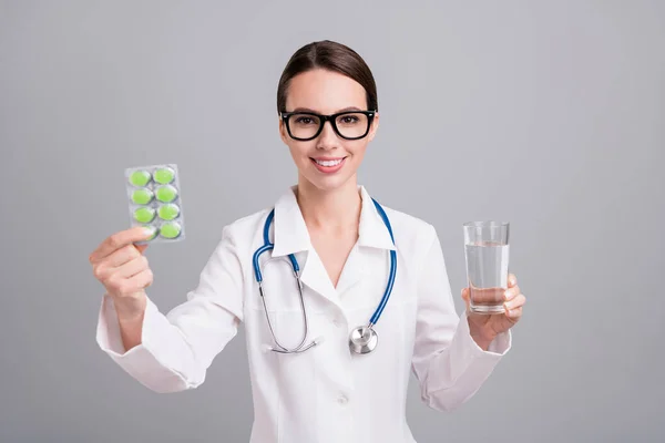 照片上漂亮甜美的医生女士身穿白衣眼镜，建议你喝独立于灰色背景的水维生素 — 图库照片