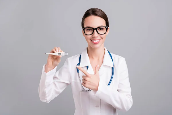 Beyaz önlük giymiş, güzel, genç bir doktor kadının fotoğrafı. Gözlükler, parmak termometresi, izole edilmiş gri arka plan. — Stok fotoğraf