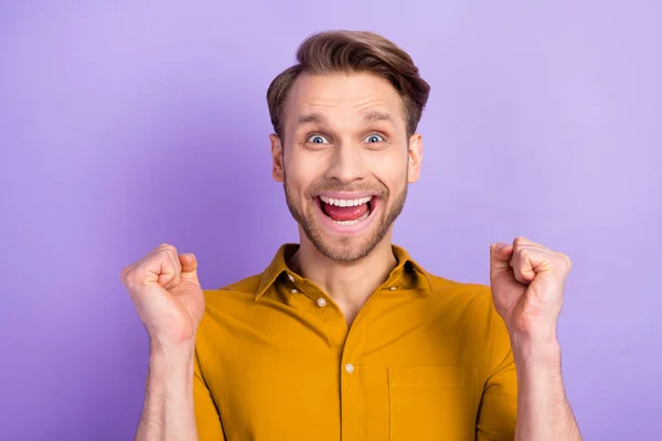 Фото щасливого чарівного молодого хлопця в повсякденному одязі, що піднімається кулаками, посміхаючись ізольованому фіолетовому кольоровому фоні — стокове фото
