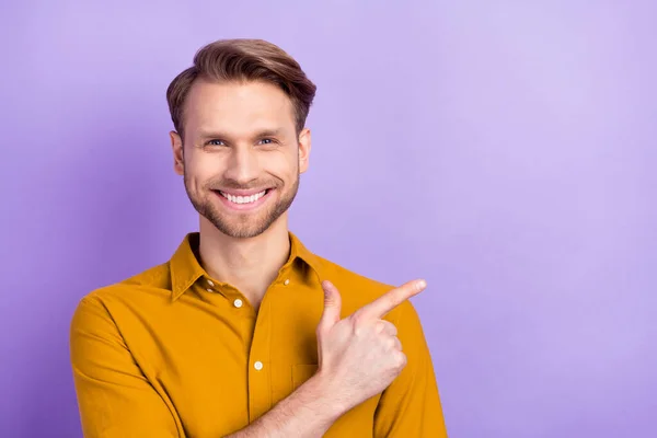 Foto retrato de un joven con camisa amarilla señalando con el dedo el espacio vacío aislado sobre fondo de color violeta brillante — Foto de Stock