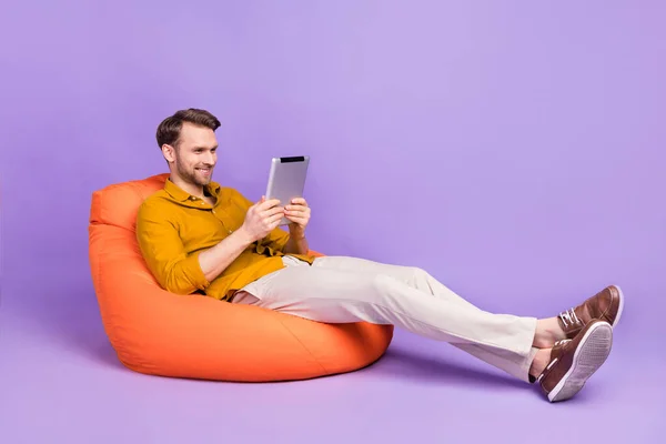 Portrait de profil pleine grandeur de gars positif assis grande chaise douce utiliser tablette isolée sur fond de couleur pourpre — Photo