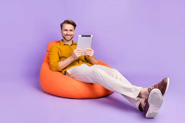 Perfil de corpo inteiro foto lateral do jovem feliz sorriso positivo uso tablet sentar cadeira feijão isolado sobre cor roxa fundo — Fotografia de Stock