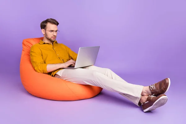 Полный профиль тела портрет серьезного спокойного человека, сидящего мягкий стул использовать ноутбук изолирован на фиолетовом фоне цвета — стоковое фото