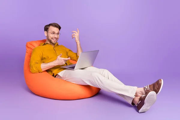 Pleine longueur taille photo de la taille du corps de gars assis dans un sac de haricot en utilisant un ordinateur portable ayant réunion vidéo isolé sur fond violet vif couleur — Photo