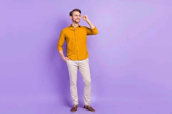 Full size photo of cheerful guy put arm in pocket touch glasses look empty space isolated on violet color background — Stock Photo, Image