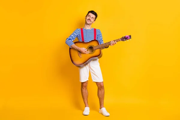 Foto de tamaño completo de joven guapo feliz positivo sonriente hombre de ensueño tocando la guitarra aislado en el fondo de color amarillo —  Fotos de Stock