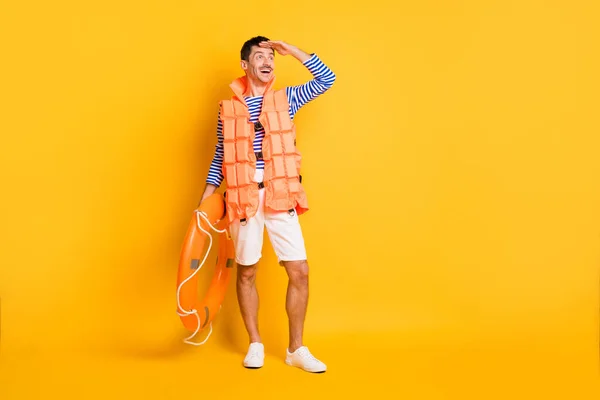 Foto corpo pieno di giovane bruna uomo sguardo copyspace usura marinaio vestito giubbotto di sicurezza tenere cerchio isolato su sfondo di colore giallo — Foto Stock