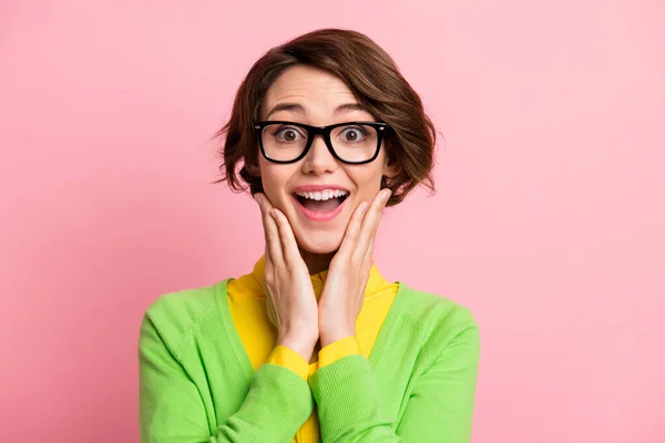 Kuva innoissaan melko nuori nainen pukeutua vihreä villatakki silmälasit auki suu kädet posket eristetty pastelli vaaleanpunainen väri tausta — kuvapankkivalokuva