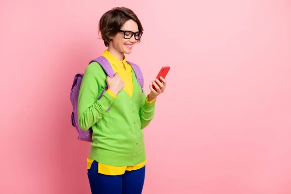 Foto de mulher brilhante usar óculos de casaco de lã verde mochila olhando gadget moderno espaço vazio isolado cor de fundo rosa — Fotografia de Stock