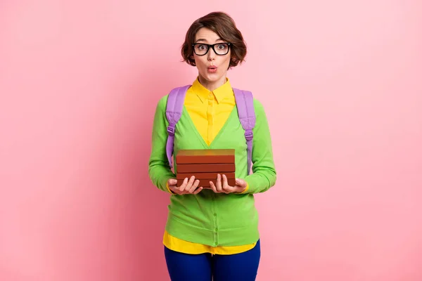 Foto de impressionado engraçado jovem mulher desgaste verde cardigan óculos mochila segurando pilha livro isolado cor rosa fundo — Fotografia de Stock