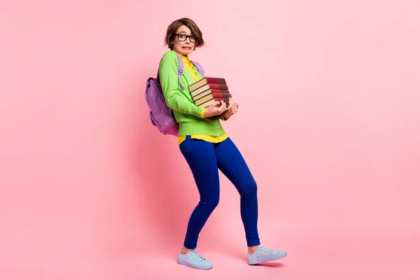 Full length photo of guilty young lady dressed yellow shirt glasses backpack walking holding book stack isolated pink color background — Stock Photo, Image