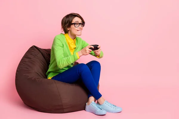 Foto em tamanho completo de funky concentrado jovem mulher jogar jogo segurar joystick sentar beanbag isolado no fundo cor-de-rosa pastel — Fotografia de Stock