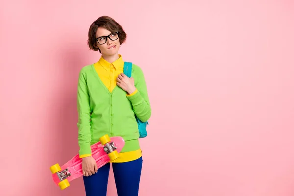Φωτογραφία του μελαχρινή ελκυστική κοπέλα εξετάσουμε κενό χώρο δάγκωμα χείλη κρατήσει skateboard φορούν μπλε παντελόνι πράσινο πουκάμισο απομονώνονται σε ροζ χρώμα φόντο — Φωτογραφία Αρχείου