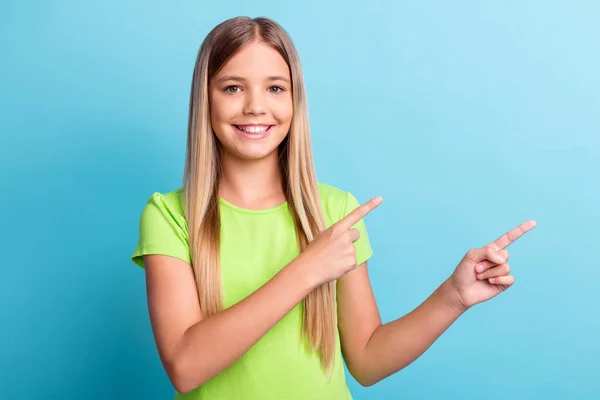 Porträtt av unga glada positiva gott humör flicka ler pekar finger i copyspace isolerad på blå färg bakgrund — Stockfoto
