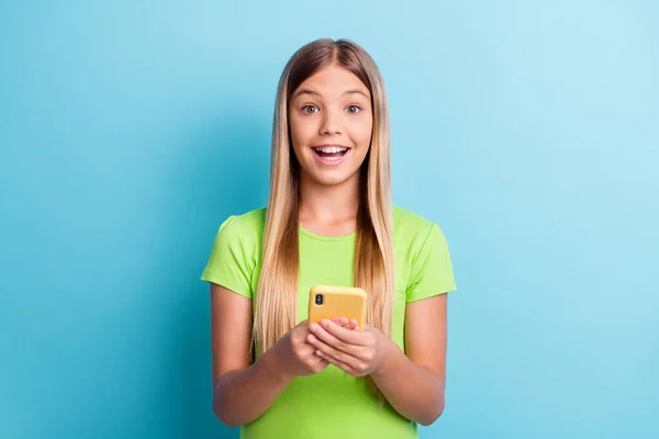 Genç, mutlu, neşeli, gülümseyen, akıllı telefon kullanan pozitif kızın fotoğrafı. Mavi arka planda yeşil tişört giy. — Stok fotoğraf