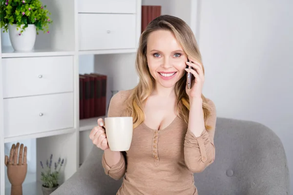 Foto di bella signora socievole seduta sedia hanno conversazione telefonica bere cacao indossare camicia beige in camera all'interno — Foto Stock