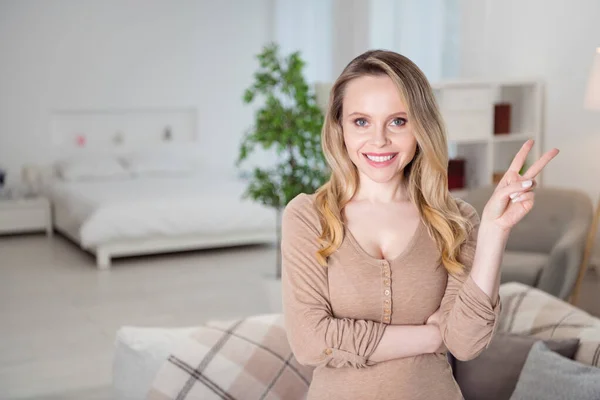 Photo of friendly lovely positive blonde lady hand show v-sign toothy smile wear beige shirt in room indoors — Φωτογραφία Αρχείου