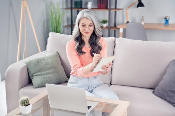 Foto de feliz encantador bonita mulher velha olhar laptop escrever nota lista plano sorriso dentro de casa casa — Fotografia de Stock