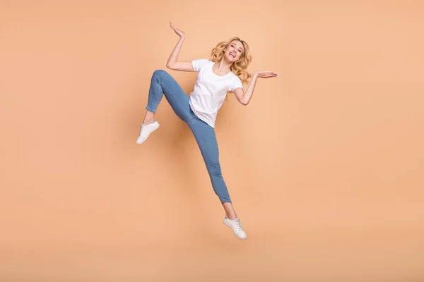 Photo of adorable pretty young woman dressed white t-shirt jumping pokazujące łuski puste miejsce uśmiechając się odizolowany beżowy kolor tła — Zdjęcie stockowe