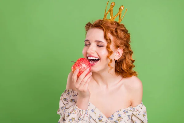 Φωτογραφία από χαρούμενα ευτυχισμένη όμορφη νεαρή γυναίκα δάγκωμα μήλο φορούν στέμμα απομονωμένο σε πράσινο φόντο χρώμα — Φωτογραφία Αρχείου