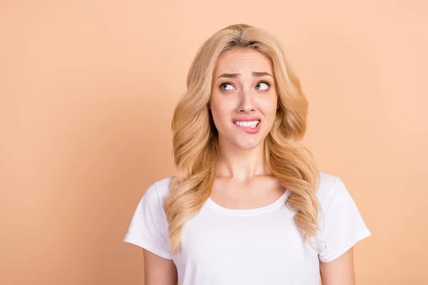 Foto retrato mujer rubia buscando espacio en blanco morder labio consiguió jalá aislado pastel color beige fondo — Foto de Stock