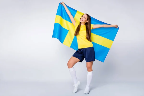 Foto de longitud completa de niña alegre positiva sostener bandera sueca apoyar a su equipo de país uefa campeón del partido de la Copa del Mundo usar zapatos kit de fútbol aislado sobre fondo de color gris — Foto de Stock