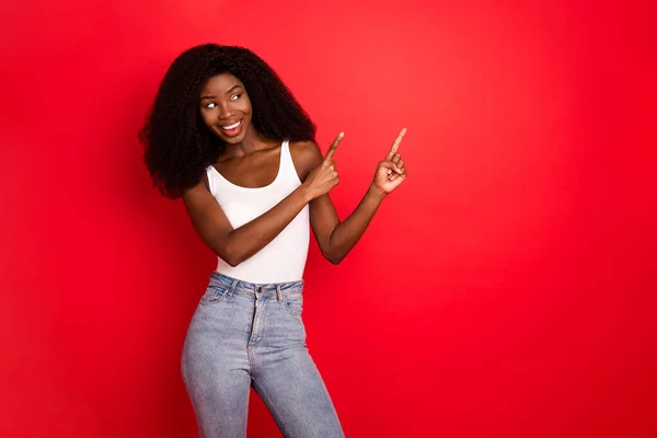 Fotografie mladé africké dívky šťastný pozitivní úsměv bod prsty prázdný prostor inzerát volba izolované nad červenou barvou pozadí — Stock fotografie