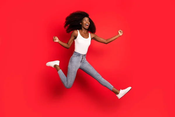 Foto em tamanho completo de jovem afro menina feliz sorriso positivo saltar para cima alegrar punhos vitória mãos isoladas sobre fundo de cor vermelha — Fotografia de Stock