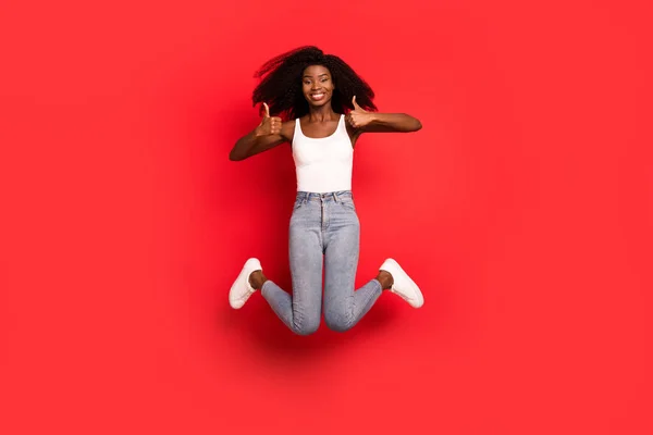 Full body foto van jong afro meisje gelukkig positieve glimlach jump up show duim-up als fijne reclame geïsoleerd over rode kleur achtergrond — Stockfoto