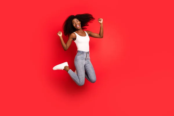 Foto de corpo inteiro de jovem afro menina feliz sorriso positivo saltar para cima alegrar punhos vitória mãos isoladas sobre fundo de cor vermelha — Fotografia de Stock