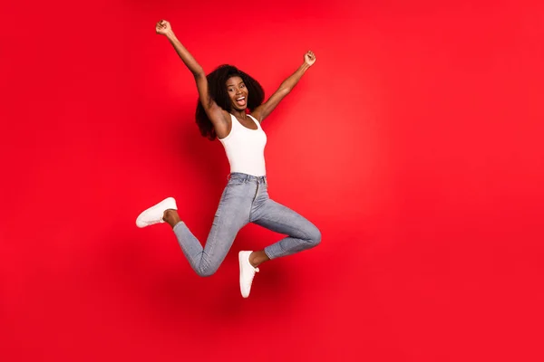 Foto de comprimento total de jovem afro menina feliz sorriso positivo saltar para cima alegrar-se ganhar sucesso sorte isolado sobre fundo de cor vermelha — Fotografia de Stock