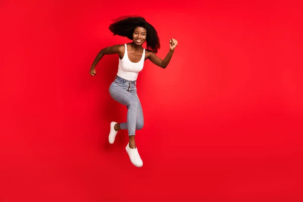 Perfil de comprimento total foto lateral da jovem afro menina feliz sorriso positivo saltar para cima ir andar corrida pressa venda isolado sobre fundo de cor vermelha — Fotografia de Stock