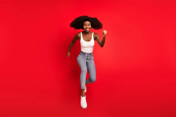 Corpo inteiro foto de jovem afro menina feliz sorriso positivo saltar para cima ir andar correr pressa isolado sobre fundo de cor vermelha — Fotografia de Stock
