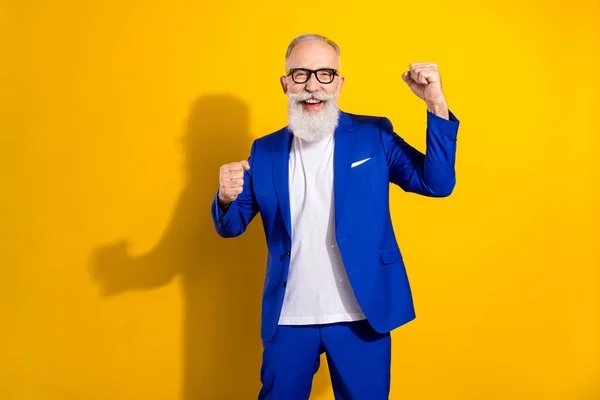 Foto de encantadoras gafas de desgaste positivas alegres levantan puños sonrisa ganadora aislada sobre fondo de color amarillo —  Fotos de Stock