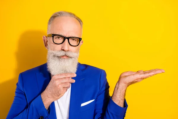 Photo of strict grey beard mature man hold empty space wear spectacles blue jacket isolated on vivid yellow color background — Stock Photo, Image