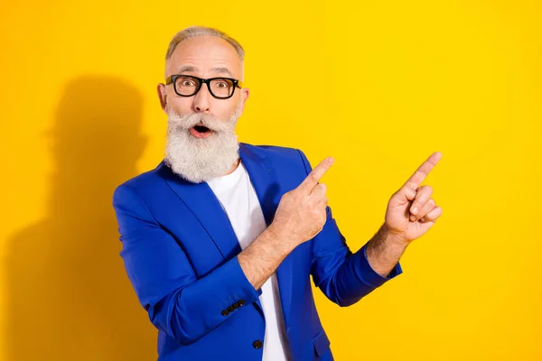 Photo portrait of senior man in blue suit amazed pointing fingers empty space isolated bright yellow color background — Stock Photo, Image