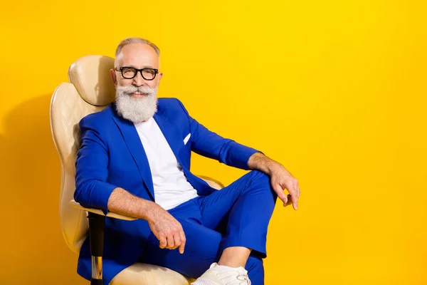 Портрет привлекательного элегантного импозантного веселого человека, сидящего в кресле директора изолированы на ярко-желтом фоне — стоковое фото