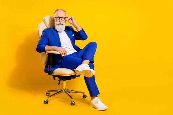 Retrato de atraente imponente homem sério sentado na cadeira tocando especificações isoladas sobre fundo de cor amarelo brilhante — Fotografia de Stock