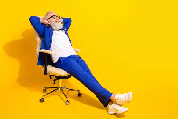 Photo pleine grandeur de bel homme d'affaires dans des lunettes assis chaise profiter du temps libre détente isolé sur fond de couleur jaune — Photo