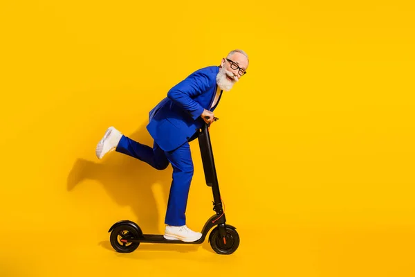 Full size profile side photo of happy smiling good mood mature man riding eco scooter isolated on yellow color background — Stock Photo, Image