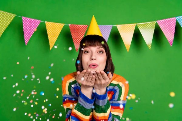 Foto di allegra giovane donna felice tenere le mani colpo coriandoli indossare cappello cono isolato su sfondo di colore verde — Foto Stock