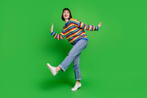 Full length φωτογραφία του γλυκού ενθουσιασμένοι νεαρή κοπέλα ντυμένος πολύχρωμο πουλόβερ χορό περπάτημα χαμογελώντας απομονωμένο πράσινο φόντο χρώμα — Φωτογραφία Αρχείου