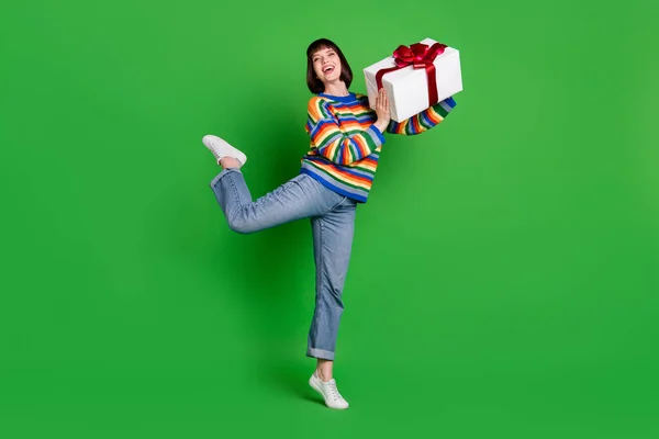 Teljes hosszúságú fotó vicces gondtalan fiatal nő visel csíkos pulóver mosolygós így ajándék doboz elszigetelt zöld színű háttér — Stock Fotó