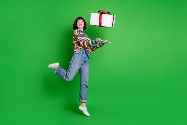 Foto de comprimento total de mulher bonito encantador usar camisola listrada sorrindo pulando jogando caixa de presente isolado fundo cor verde — Fotografia de Stock