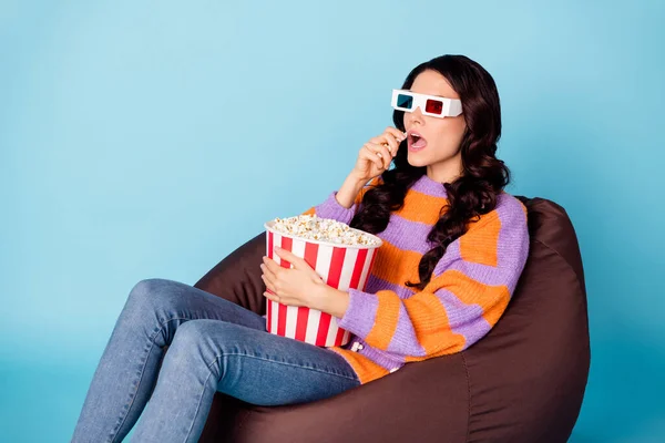 Porträt eines attraktiven welligen Mädchens, das auf einem Stuhl sitzt und sich den Film ansieht, wie es Mais isst und seine Freizeit isoliert auf hellblauem Hintergrund verbringt — Stockfoto