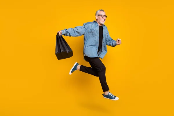 Teljes test profil fotó vicces nagypapa hold táskák futtatni kopás kabát nadrág elszigetelt sárga színű háttér — Stock Fotó