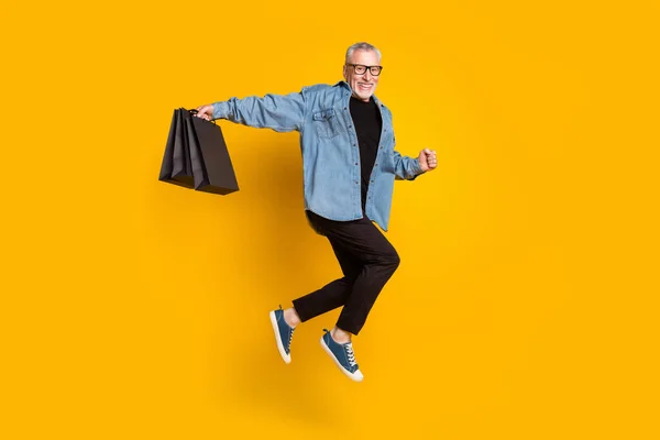 Pleine taille photo de profil de funky grand-père tenir des sacs saut porter pantalon veste isolé sur fond de couleur jaune — Photo