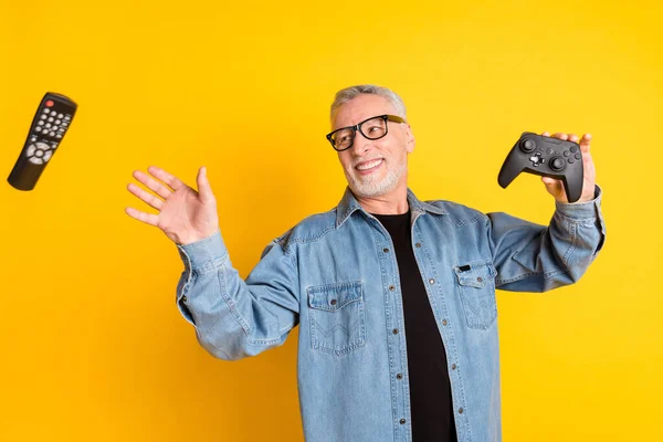 Foto de sensación divertida joven abuelo captura consola usar gafas jeans chaqueta aislada sobre fondo de color amarillo — Foto de Stock