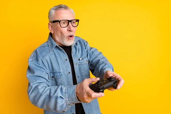 Photo of impressed feel young grandpa play video game wear eyewear jeans jacket isolated on yellow color background — ストック写真